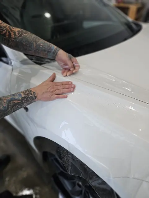 Installer laying clear paint protection film over the paint of a white car