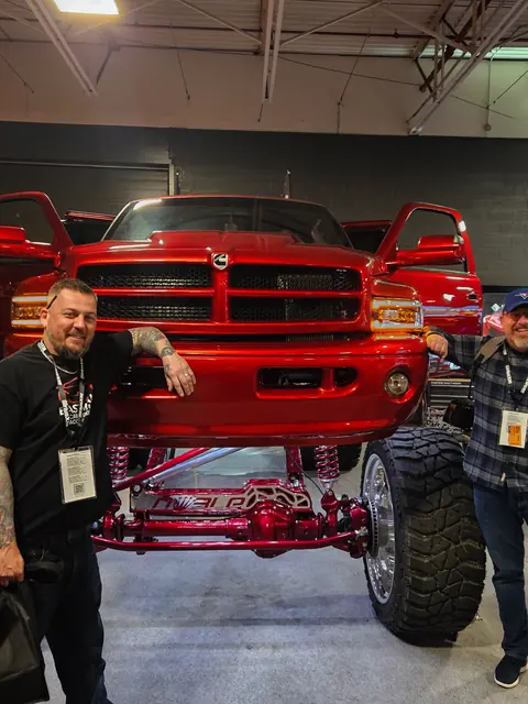 Two men standing beside a lifted red Dodge Ram on a show floor